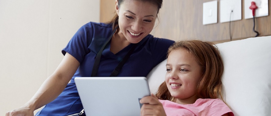nurse smiling with pediatric girl patient who is looking at a tablet device