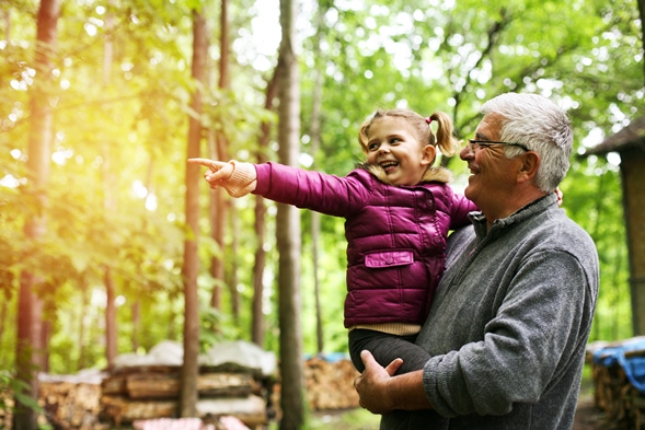 Grandfather and granddaughter smiling in forest of trees